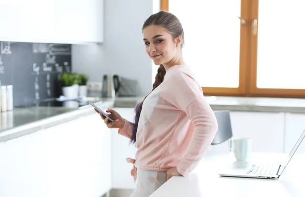 Vrouw met behulp van mobiele telefoon staande in de moderne keuken. — Stockfoto