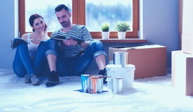 Yeni evin içini boyayan mutlu, gülümseyen genç bir çift portresi. Genç çift