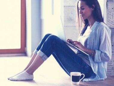 Dizüstü bilgisayar ile yerdeki genç güzel kadın evde oturuyor. Genç güzel kadın.