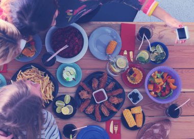 Ahşap masada otururken birlikte yemek yiyen bir grup insanın üst düzey görüntüsü. Masada yemek var. İnsanlar fast food yiyor..