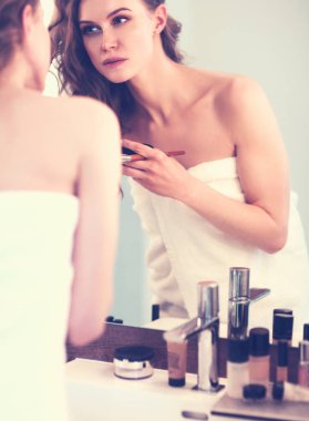 Genç bir kadın aynaya bakıyor ve makyaj yapıyor..