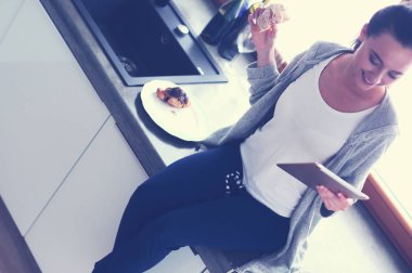 Mutfakta dijital tablet kullanan güzel genç bir kadın.