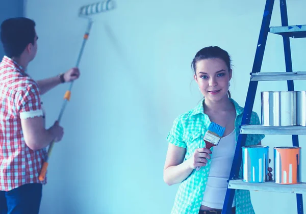 Retrato de feliz joven pareja sonriente pintando la pared interior de la nueva casa — Foto de Stock