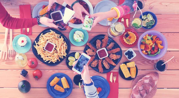 Ahşap masada otururken birlikte yemek yiyen bir grup insanın üst düzey görüntüsü. Masada yemek var. İnsanlar fast food yiyor. Yemek fotoğrafı.