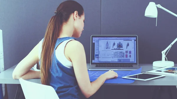 Ung kvinna sitter vid skrivbordet med instrument, plan och laptop — Stockfoto