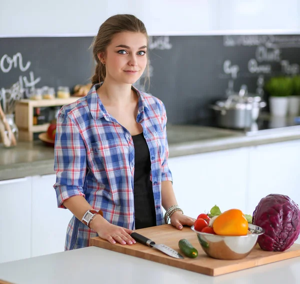 Masanın yanındaki mutfakta sebze doğrayan genç bir kadın..