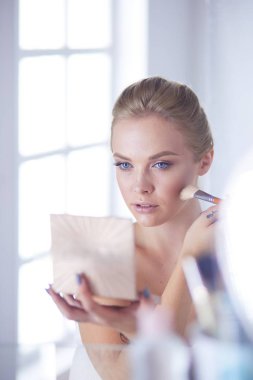 Genç bir kadının banyoya yüz pudrası sürerken fotoğrafı.