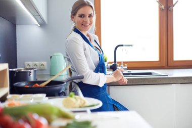 Mutfakta sobanın yanında duran genç bir kadın.