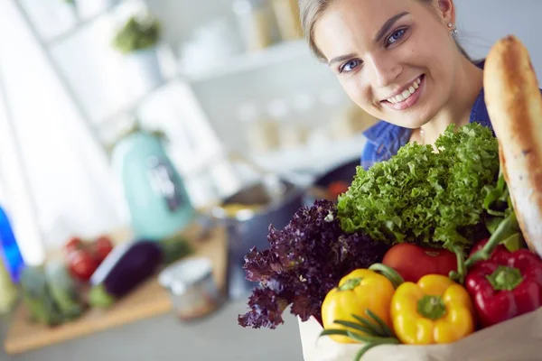 Giovane donna che tiene borsa della spesa con verdure. In piedi in cucina — Foto Stock