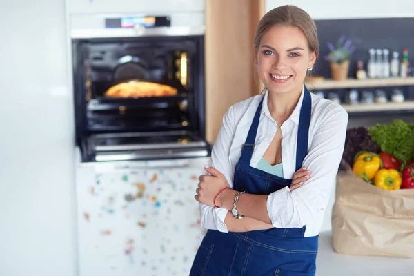 Portrét mladé ženy stojící s rukama zkříženýma na pozadí kuchyně — Stock fotografie
