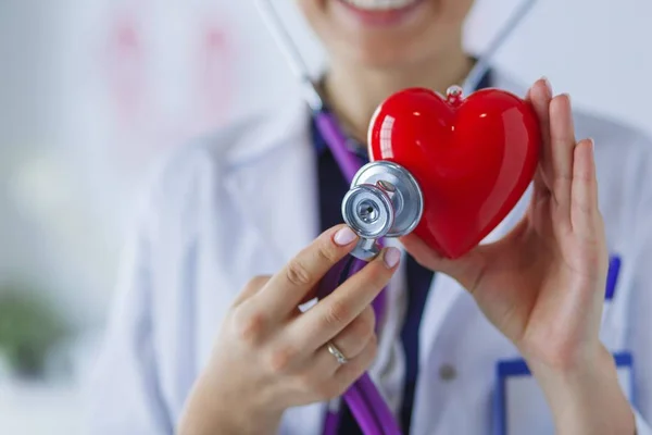 Un médico con estetoscopio examinando el corazón rojo, aislado sobre fondo blanco —  Fotos de Stock
