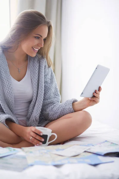 Entspannte junge Frau sitzt mit einer Tasse Kaffee und digitalem Tablet im Bett — Stockfoto