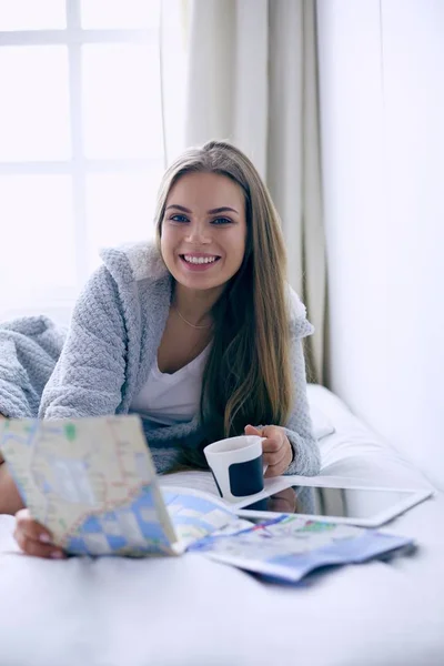 Giovane donna rilassata seduta sul letto con una tazza di caffè e tablet digitale — Foto Stock