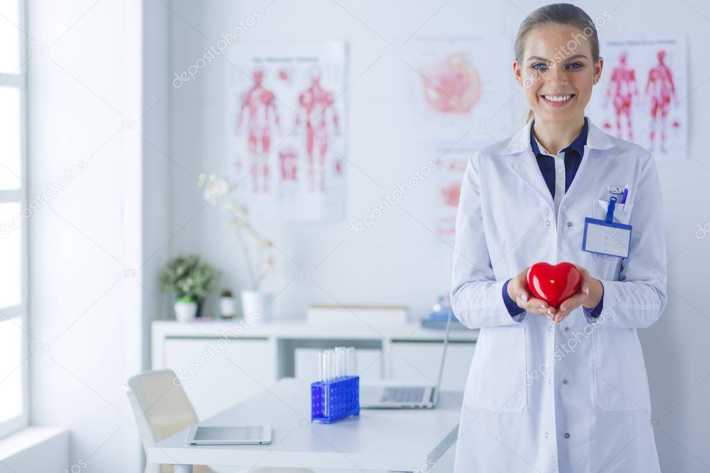 A doctor with stethoscope examining red heart, isolated on white background