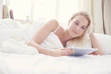 Elinde boş ekranlı dijital tablet tutan ve yatak odasında kameraya gülümseyen bir kız.