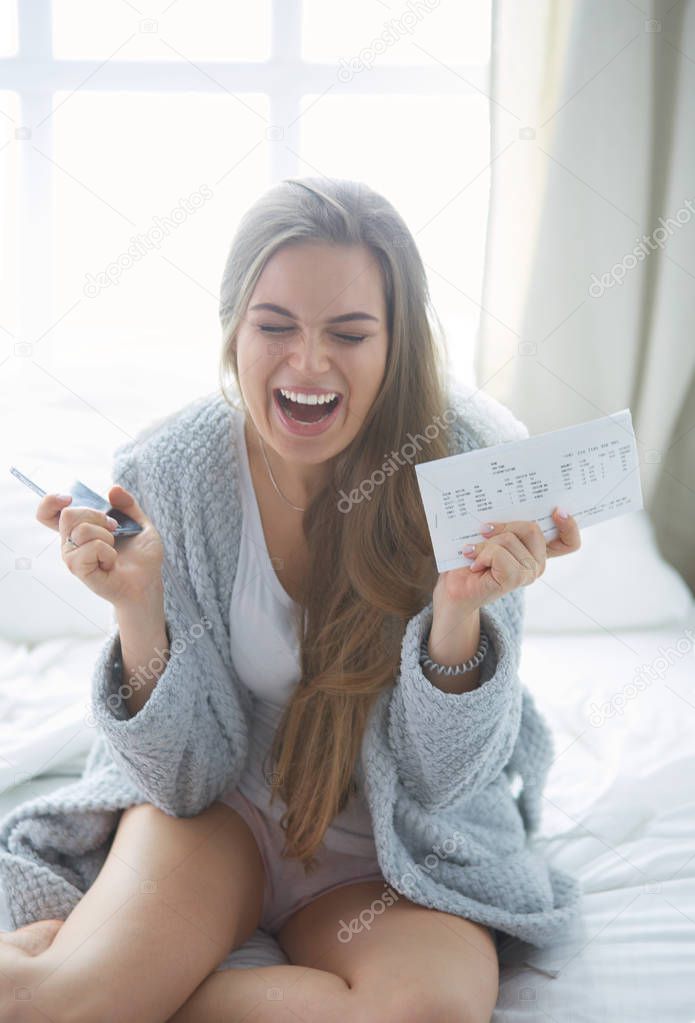 Relaxed young woman sitting on bed with a cup of coffee and digital tablet