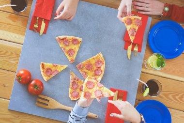 Ahşap masada otururken birlikte yemek yiyen bir grup insanın üst düzey görüntüsü. Masada yemek var. İnsanlar fast food yiyor..