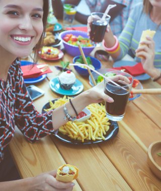 Ahşap masada otururken birlikte yemek yiyen bir grup insanın üst düzey görüntüsü. Masada yemek var. İnsanlar fast food yiyor..