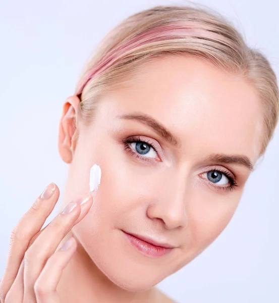 Portrait de belle jeune femme souriante heureuse touchant la peau ou appliquant de la crème, isolée sur fond blanc — Photo