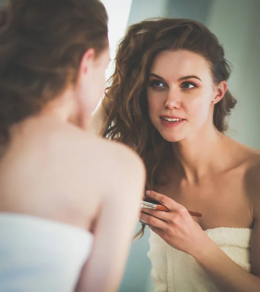Fiatal nő néz a tükörbe, és smink fel. — Stock Fotó
