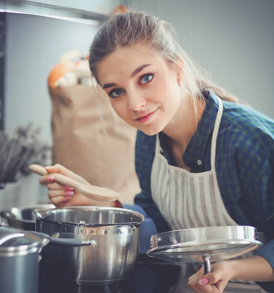 Νεαρή γυναίκα μαγειρεύει στην κουζίνα της στέκεται κοντά στο φούρνο — Φωτογραφία Αρχείου