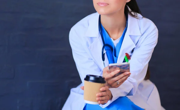Női orvos ül a mobiltelefon és kávézás — Stock Fotó