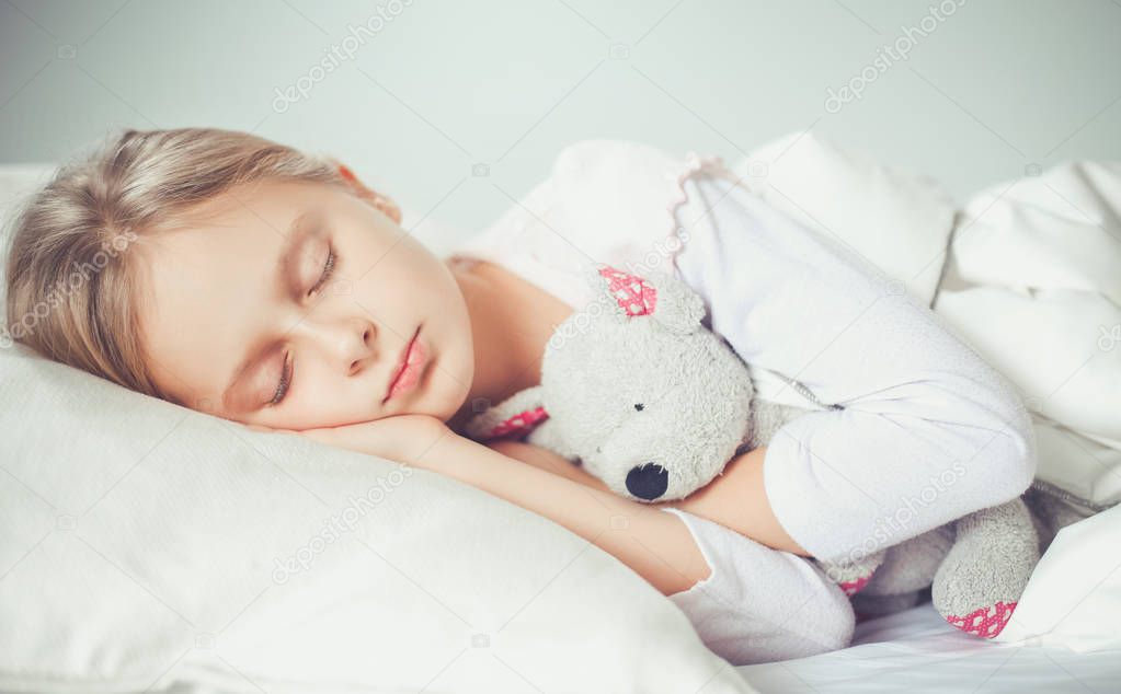 Child little girl sleeps in the bed with a toy teddy bear