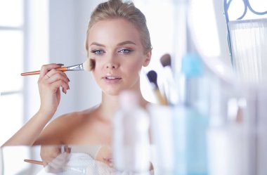 Genç bir kadının banyoya yüz pudrası sürerken fotoğrafı.