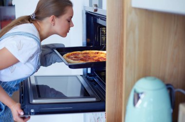 Mutlu genç bayan evde pizza pişiriyor.