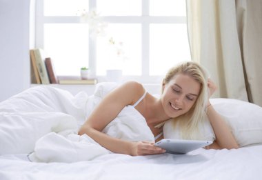 Elinde boş ekranlı dijital tablet tutan ve yatak odasında kameraya gülümseyen bir kız.