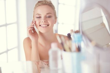 Bornozlu genç kadın banyo aynasına bakıyor.