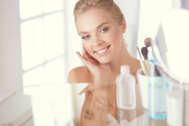 Bornozlu genç kadın banyo aynasına bakıyor.