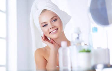 Bornozlu genç kadın banyo aynasına bakıyor.