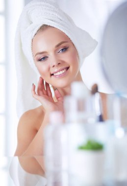 Bornozlu genç kadın banyo aynasına bakıyor.