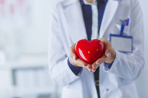 Jeune femme médecin tenant un cœur rouge, debout sur fond d'hôpital — Photo