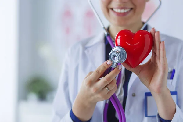 Un médecin avec stéthoscope examinant le cœur rouge, isolé sur fond blanc — Photo