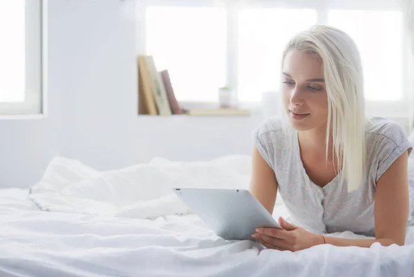 Chica sosteniendo tableta digital con pantalla en blanco y sonriendo a la cámara en el dormitorio — Foto de Stock