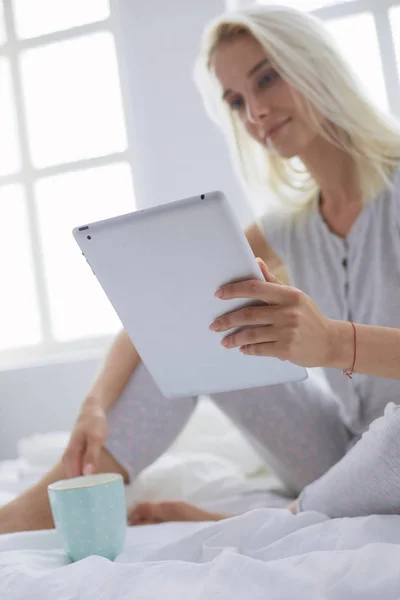 Chica sosteniendo tableta digital con pantalla en blanco y sonriendo a la cámara en el dormitorio — Foto de Stock