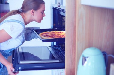 Mutlu genç bayan evde pizza pişiriyor.