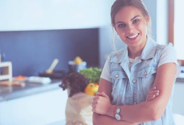 Kollarını mutfak arka planında kavuşturmuş genç bir kadının portresi.