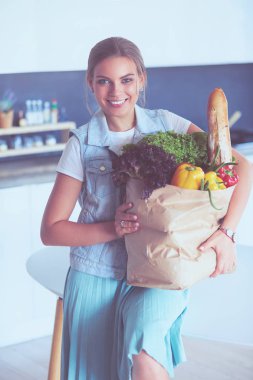 Sebzeli alışveriş poşeti taşıyan genç bir kadın. Mutfakta duruyor..