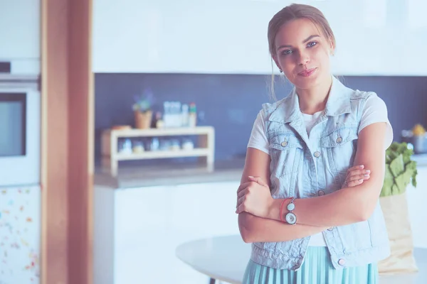 Portrait of young woman standing with arms crossed against kitchen background — Stock Photo, Image