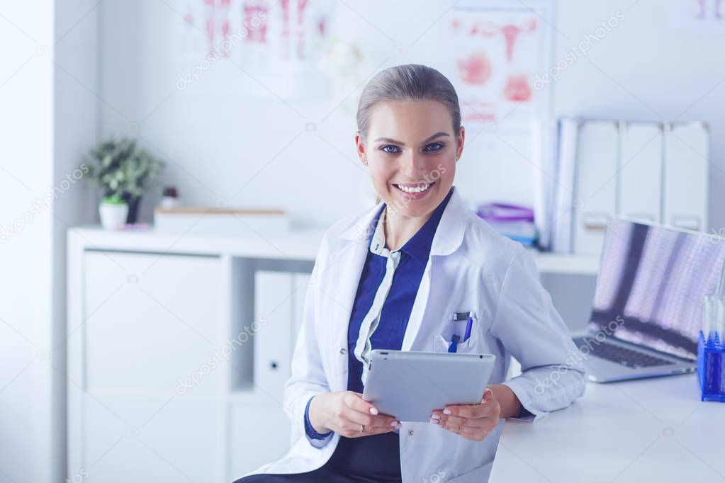 Portrait of woman doctor at hospital corridor, holding tablet computer, looking at camera, smiling