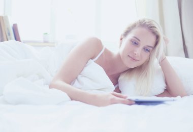 Elinde boş ekranlı dijital tablet tutan ve yatak odasında kameraya gülümseyen bir kız.