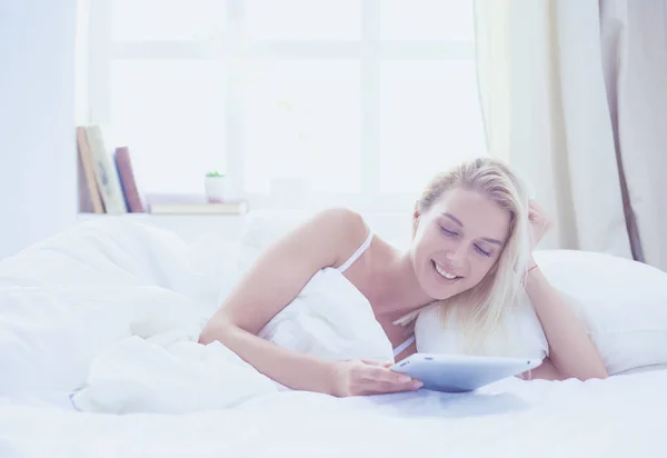 Menina segurando tablet digital com tela em branco e sorrindo para a câmera no quarto — Fotografia de Stock