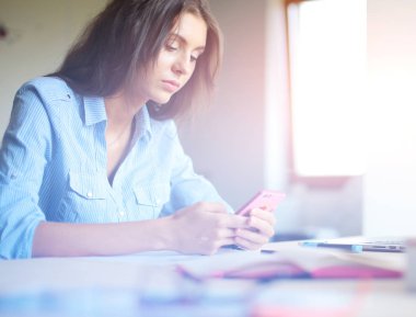 Ofis masasında oturan ve cep telefonuyla konuşan genç ve güzel bir iş kadını. İş kadını