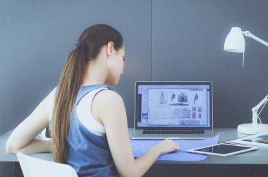 Masasında enstrümanlar, planlar ve dizüstü bilgisayarlarla oturan genç bir kadın.