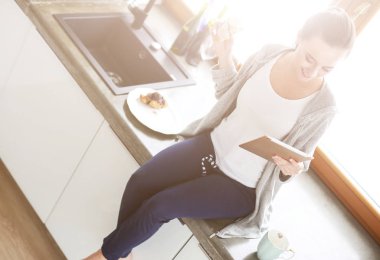 Mutfakta dijital tablet kullanan güzel genç bir kadın..