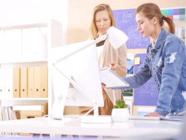 Masanın yanında duran iki genç kadın enstrüman, plan ve dizüstü bilgisayarla.