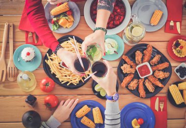 Ahşap masada otururken birlikte yemek yiyen bir grup insanın üst düzey görüntüsü. Masada yemek var. İnsanlar fast food yiyor..